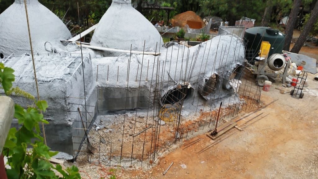 Gray cement-sprayed domes and a vaulted tunnel with vertical rebar rising around the footing, a cement mixer behind