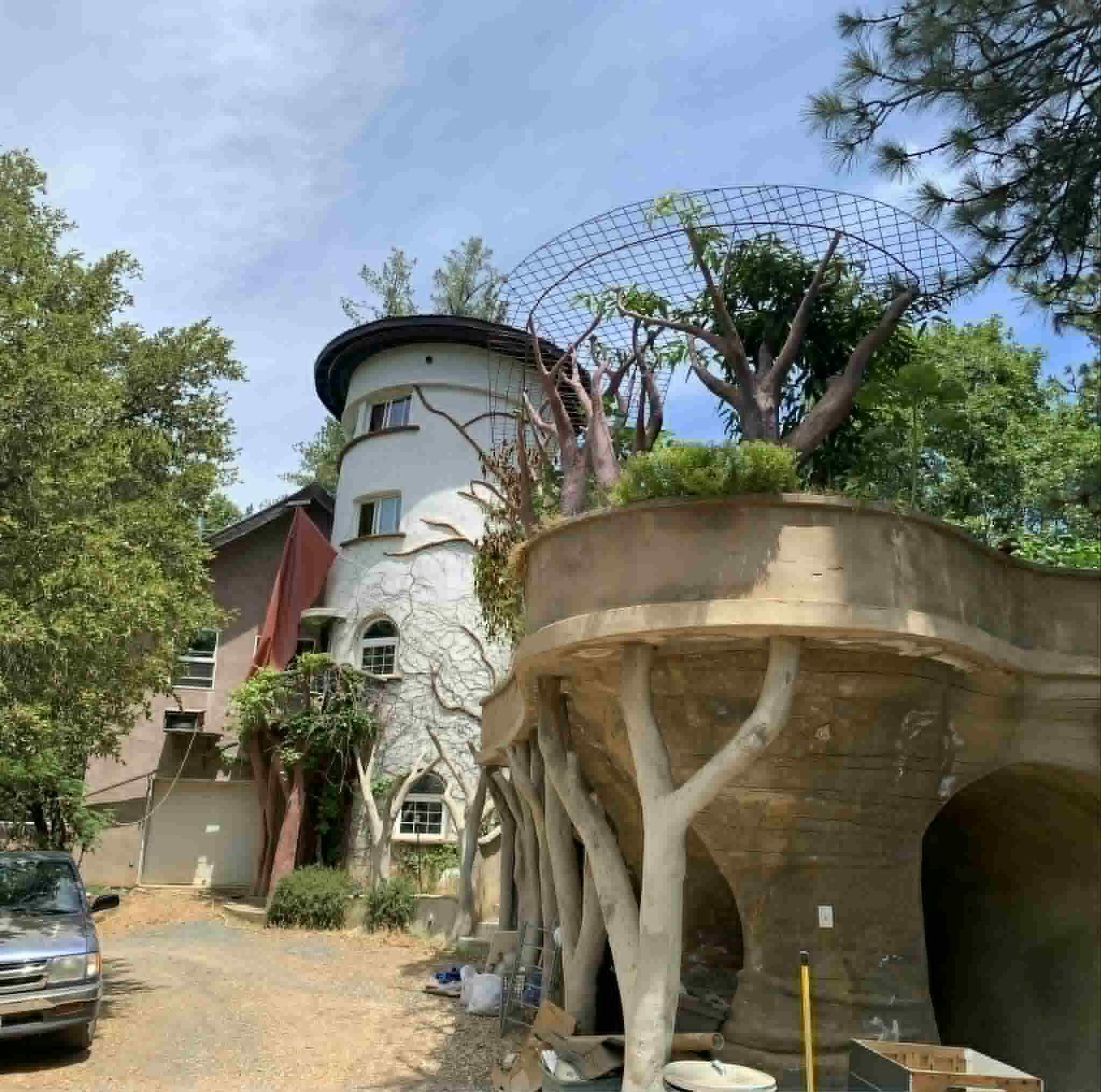 A white tower with tree-branch relief beside a curving planter deck carried on sculpted tree columns
