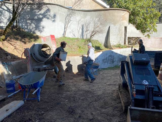Guild volunteers hauling buckets of mix from a cement mixer beside a curved ferro-cement wall